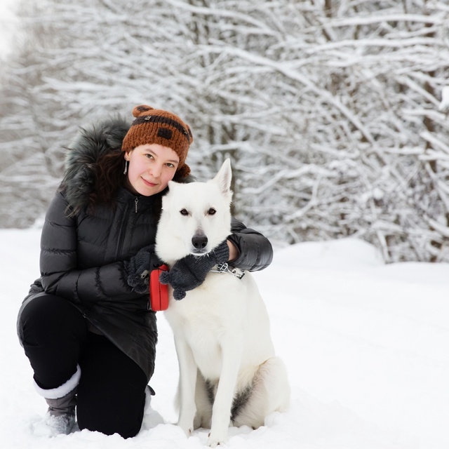 Ein weißer Schäferhund neben einem Menschen im Wald, unter dem Schnee